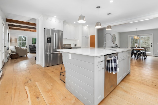 kitchen featuring a sink, beamed ceiling, appliances with stainless steel finishes, and light wood-style flooring