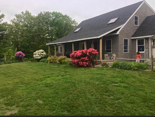 back of house with a lawn, covered porch, and a shingled roof