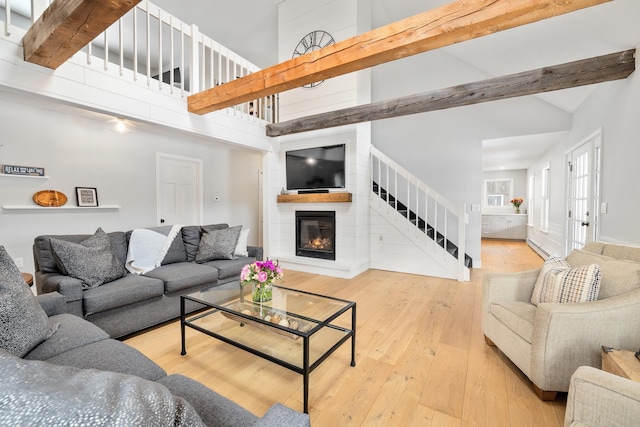 living area featuring high vaulted ceiling, a fireplace, stairs, wood-type flooring, and beamed ceiling