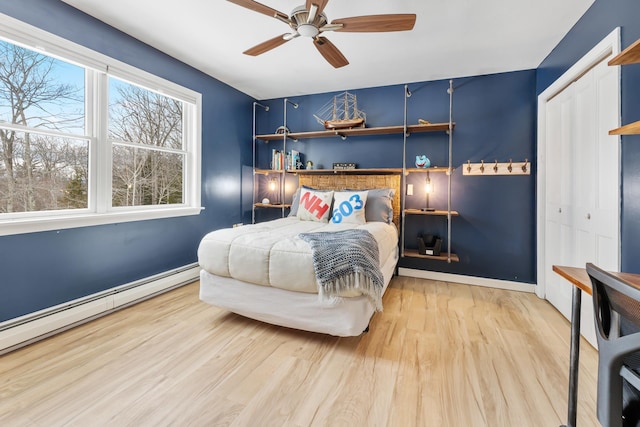 bedroom with a closet, light wood-style floors, a baseboard radiator, baseboards, and ceiling fan