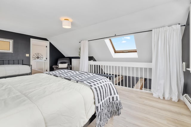 bedroom with baseboard heating, vaulted ceiling with skylight, and wood finished floors