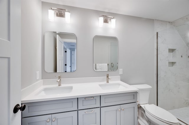 bathroom featuring double vanity, toilet, a tile shower, and a sink