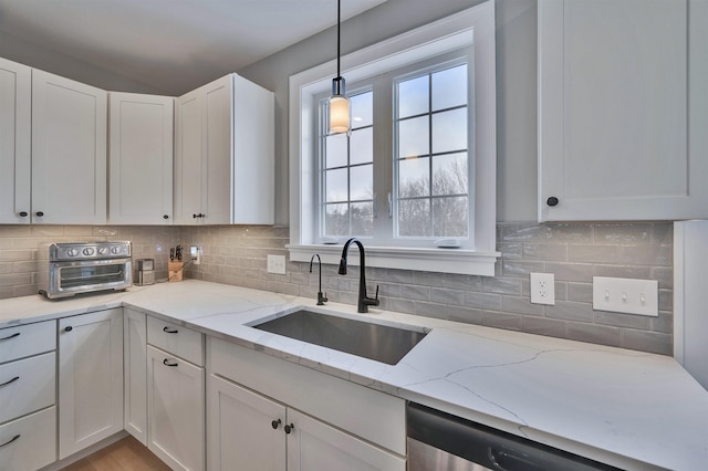 kitchen with stainless steel dishwasher, decorative backsplash, white cabinetry, and a sink