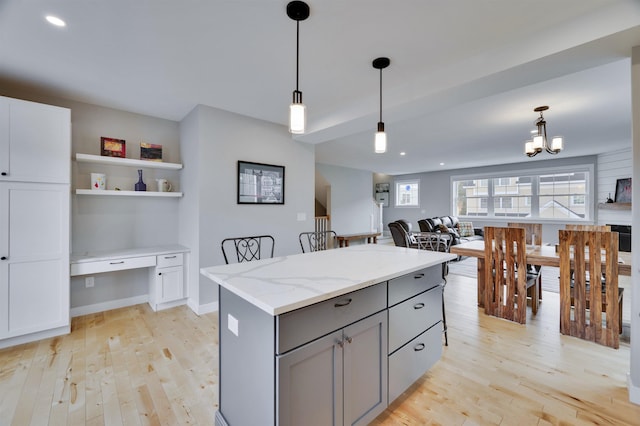 kitchen with gray cabinetry, a kitchen island, pendant lighting, light wood-style floors, and built in study area