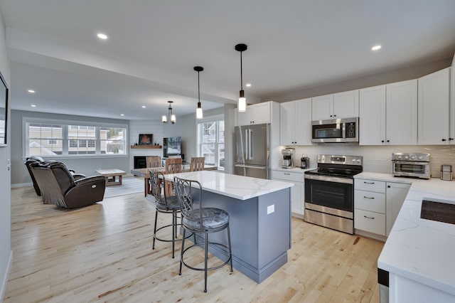 kitchen with light wood-type flooring, a breakfast bar, a fireplace, appliances with stainless steel finishes, and open floor plan