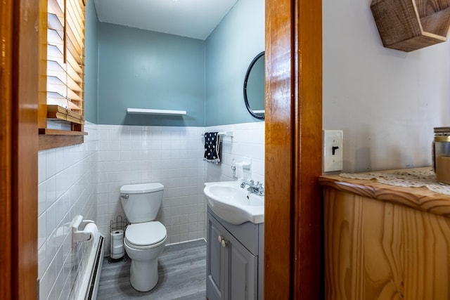 half bathroom with tile walls, toilet, wainscoting, wood finished floors, and vanity