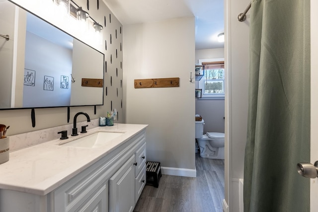 bathroom with toilet, vanity, baseboards, and wood finished floors