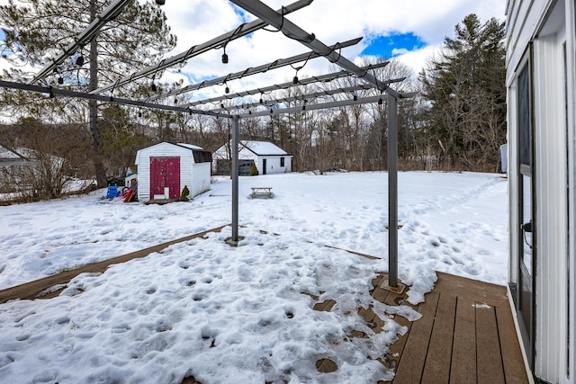 snowy yard with a shed, a pergola, and an outdoor structure