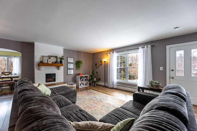 living area with arched walkways, baseboard heating, a large fireplace, and wood finished floors