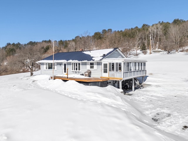 snow covered back of property with a deck, metal roof, and a standing seam roof