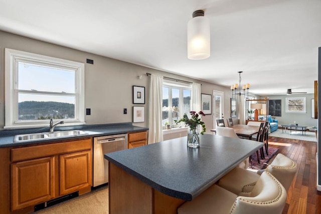 kitchen with brown cabinets, a sink, stainless steel dishwasher, dark countertops, and a breakfast bar area