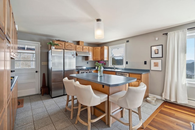 kitchen with under cabinet range hood, a sink, dark countertops, freestanding refrigerator, and range