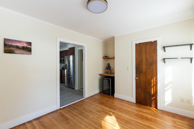 unfurnished room featuring wine cooler, baseboards, crown molding, and light wood-style floors