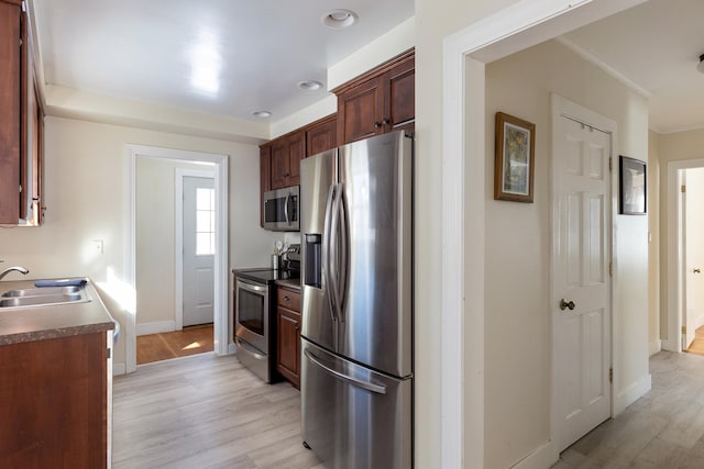 kitchen with baseboards, a sink, stainless steel appliances, light wood-style floors, and dark countertops