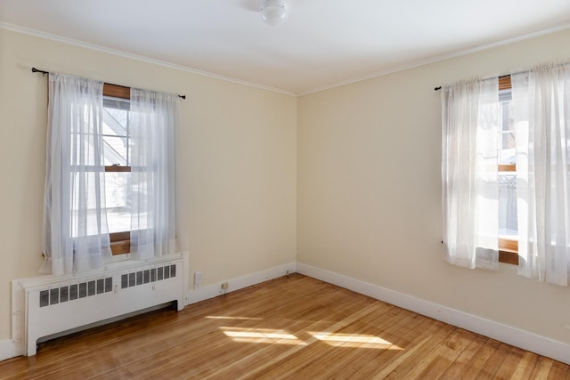 empty room with baseboards, light wood-style flooring, radiator heating unit, and crown molding