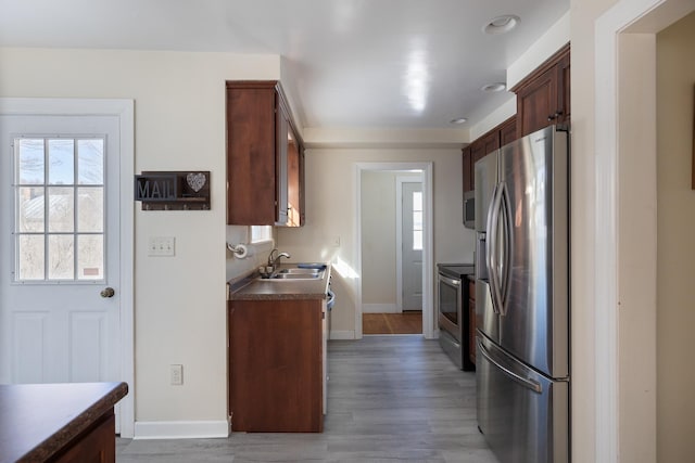 kitchen with a sink, stainless steel appliances, light wood-type flooring, and baseboards