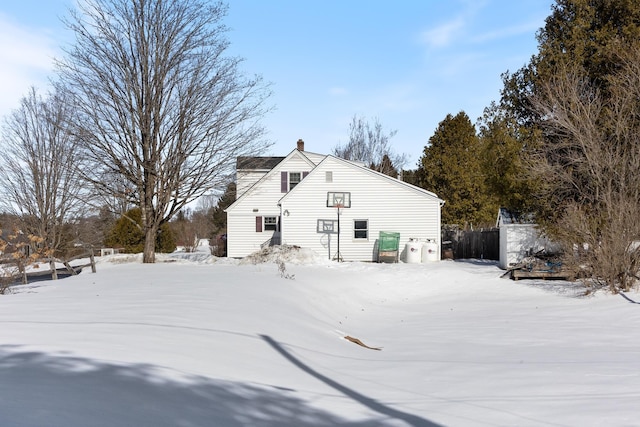 snow covered house featuring a chimney and fence