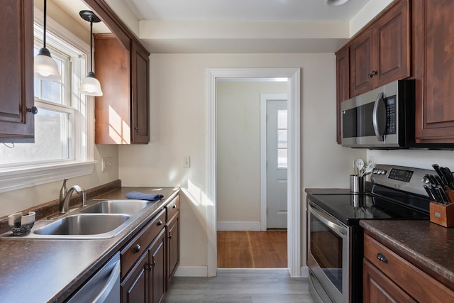 kitchen featuring a sink, stainless steel appliances, dark countertops, and light wood-style flooring