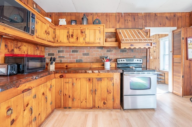 kitchen with light wood-style flooring, appliances with stainless steel finishes, wood walls, and exhaust hood