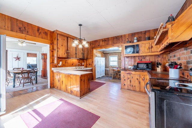 kitchen with electric range, light wood-style flooring, wood walls, brown cabinetry, and black microwave