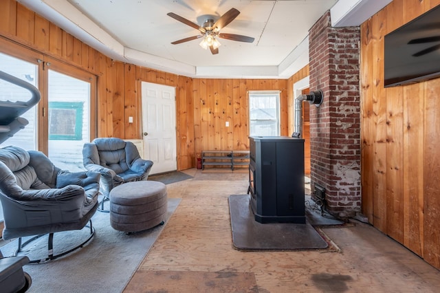 living area with ceiling fan, a healthy amount of sunlight, wood walls, and a wood stove