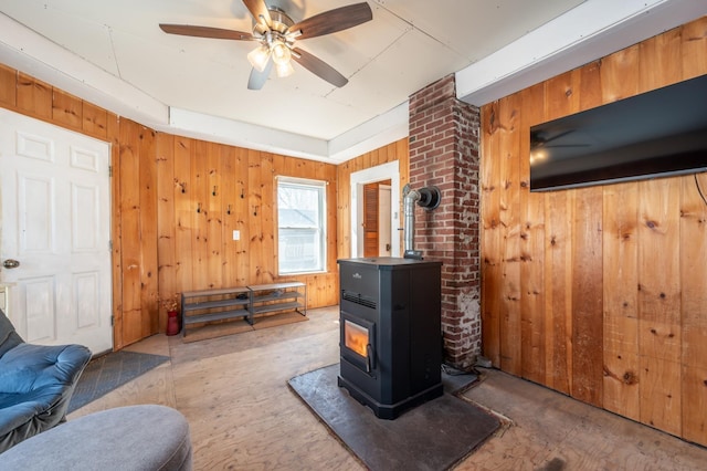 living room with ceiling fan, wood walls, and a wood stove