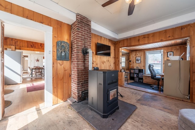 living room featuring a wood stove, wooden walls, and ceiling fan