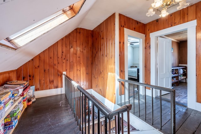 hall with an upstairs landing, wooden walls, hardwood / wood-style floors, and vaulted ceiling with skylight