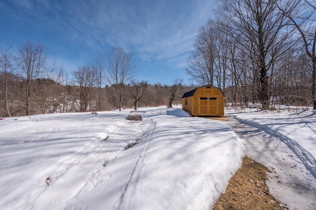 snowy yard with an outbuilding, a view of trees, and a shed