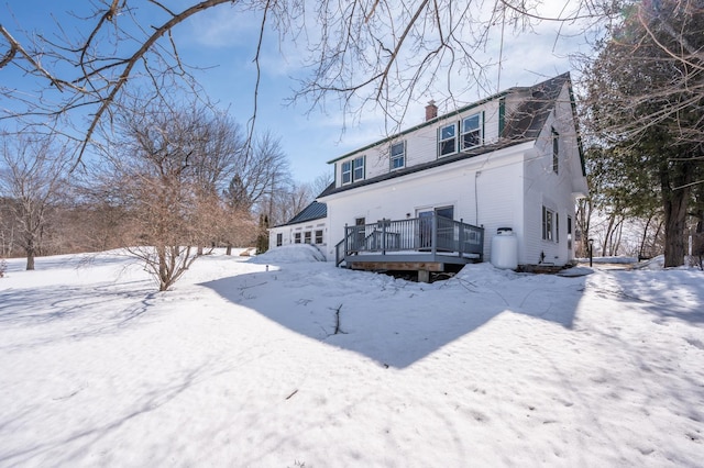 snow covered house with a wooden deck and a chimney