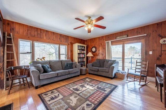 living room with a ceiling fan, visible vents, wood walls, and light wood-type flooring