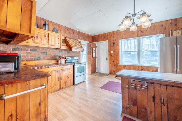 kitchen with custom exhaust hood, wooden walls, appliances with stainless steel finishes, and light wood-style floors