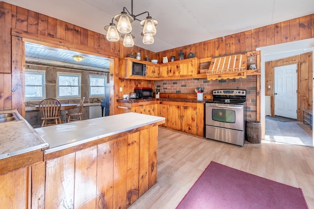 kitchen with light wood-type flooring, stainless steel range with electric cooktop, wood walls, black microwave, and extractor fan