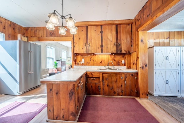 kitchen with a peninsula, a sink, light countertops, wood walls, and high end refrigerator