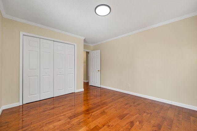 unfurnished bedroom featuring a closet, crown molding, baseboards, and hardwood / wood-style flooring