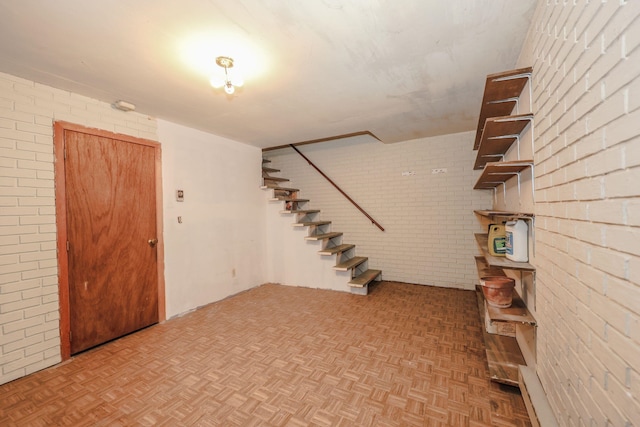 finished below grade area featuring parquet floors, brick wall, and stairs