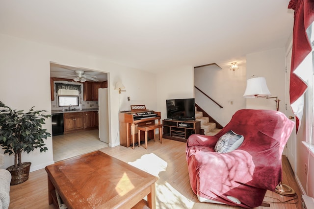 living area featuring stairway, light wood-style flooring, and a ceiling fan