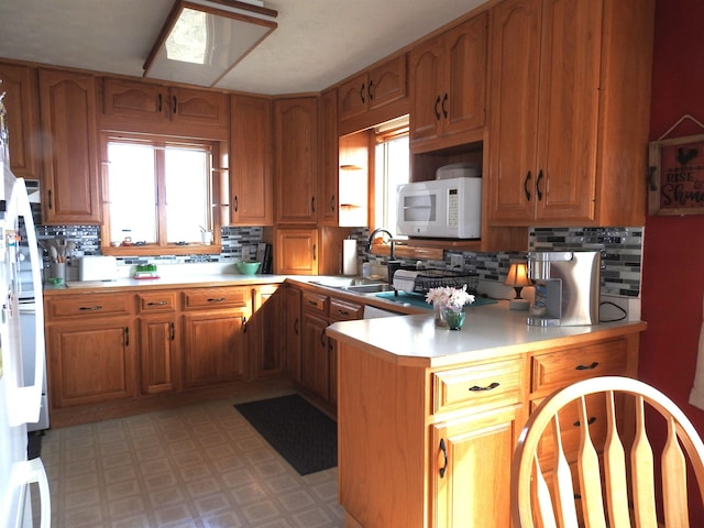 kitchen featuring white microwave, light floors, light countertops, a peninsula, and a sink