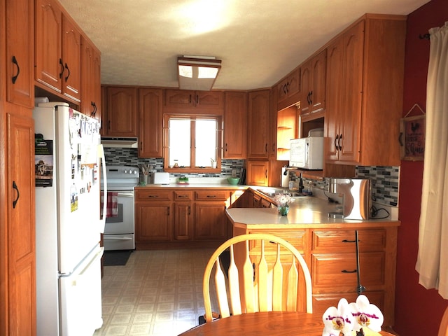 kitchen featuring light floors, light countertops, brown cabinetry, white appliances, and a sink