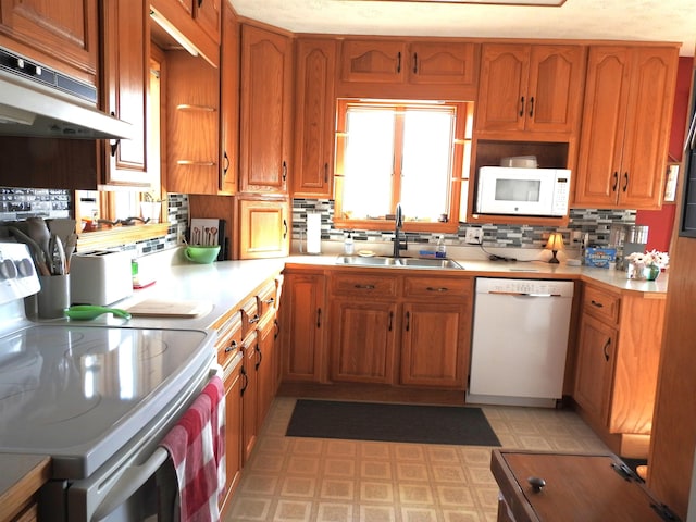 kitchen featuring under cabinet range hood, a sink, white appliances, light countertops, and light floors