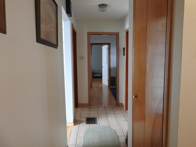 hallway featuring light tile patterned floors, baseboards, and visible vents