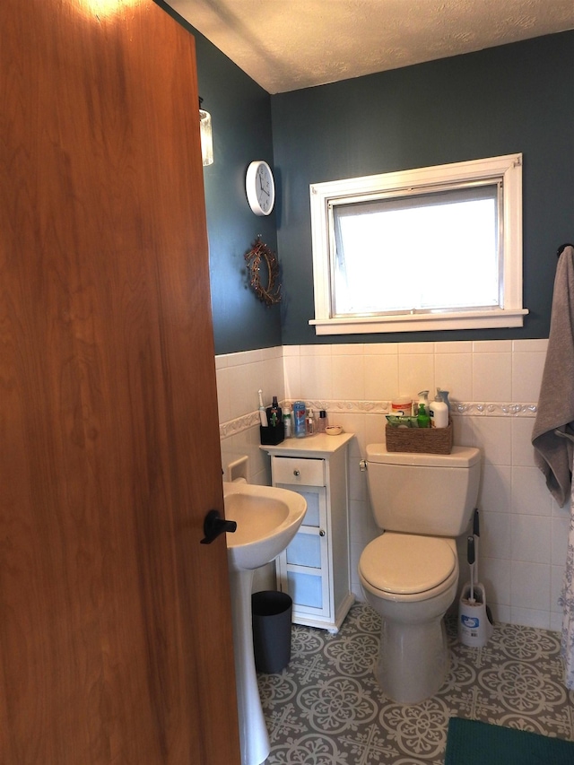 bathroom with tile walls, toilet, wainscoting, tile patterned floors, and a textured ceiling