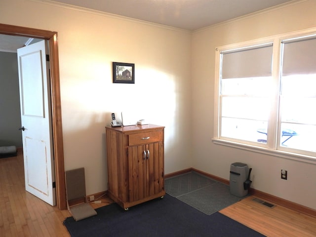 interior space with visible vents, light wood-style flooring, baseboards, and ornamental molding