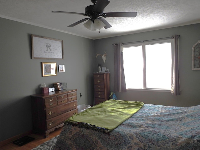 bedroom featuring ceiling fan, a textured ceiling, wood finished floors, and ornamental molding