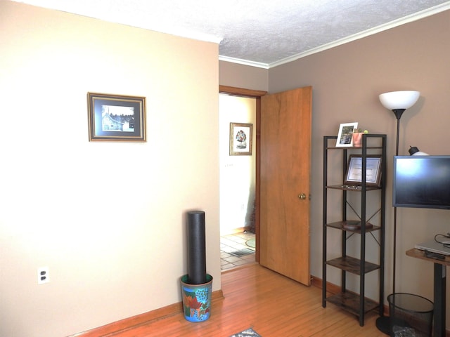 interior space with crown molding, wood finished floors, baseboards, and a textured ceiling