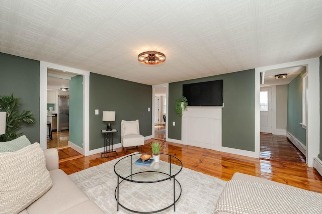 living room with a baseboard heating unit, baseboards, and wood finished floors