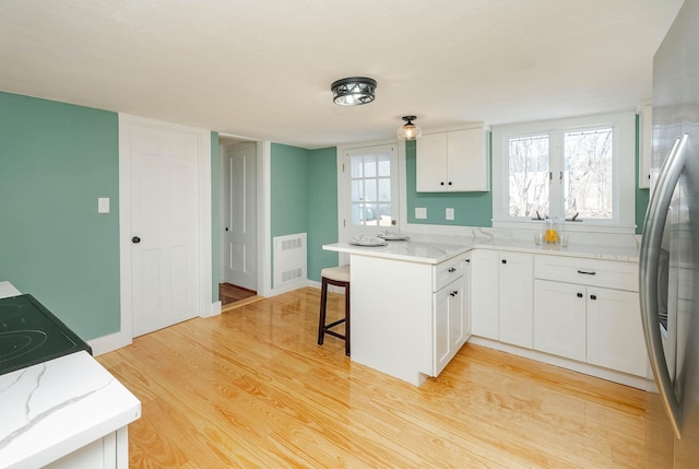 kitchen with visible vents, light wood-type flooring, white cabinetry, freestanding refrigerator, and a peninsula