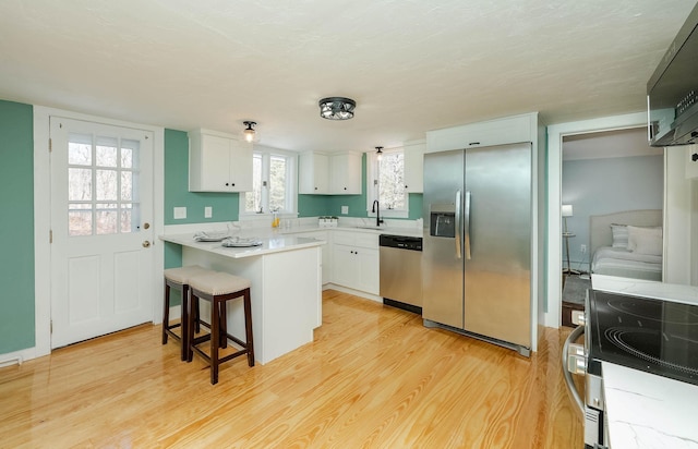 kitchen featuring a peninsula, a sink, stainless steel appliances, light countertops, and light wood-type flooring