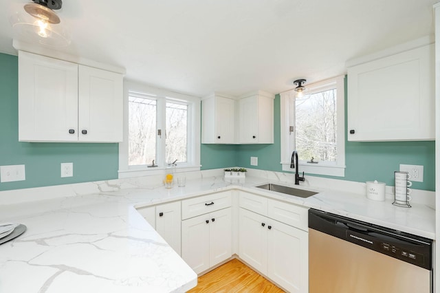 kitchen with light stone counters, a sink, white cabinets, stainless steel dishwasher, and light wood-type flooring