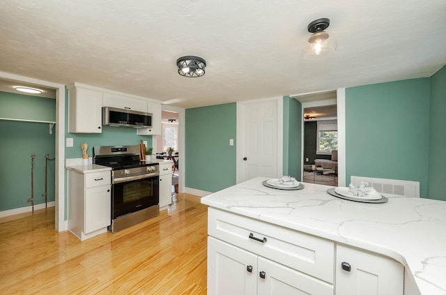 kitchen featuring light stone counters, baseboards, light wood finished floors, appliances with stainless steel finishes, and white cabinetry